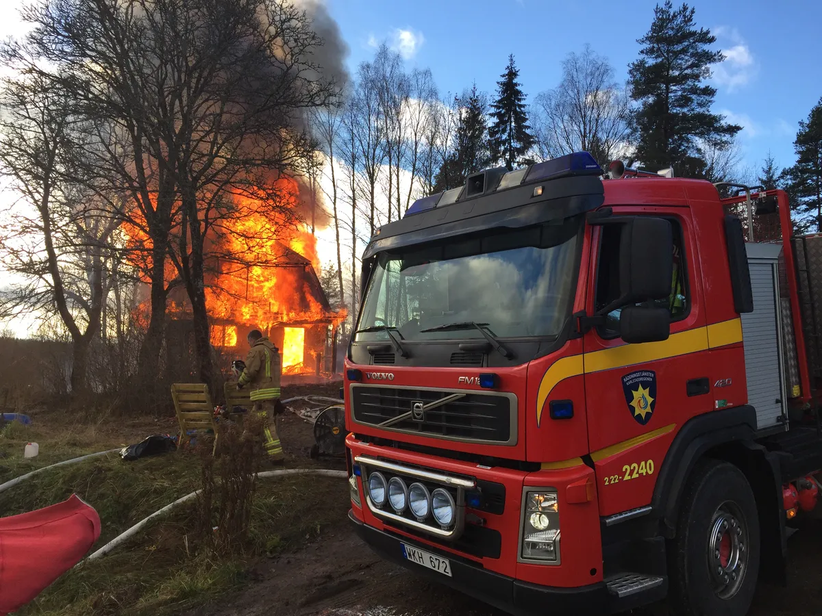 Fire truck in front of burning wooden house with high flames