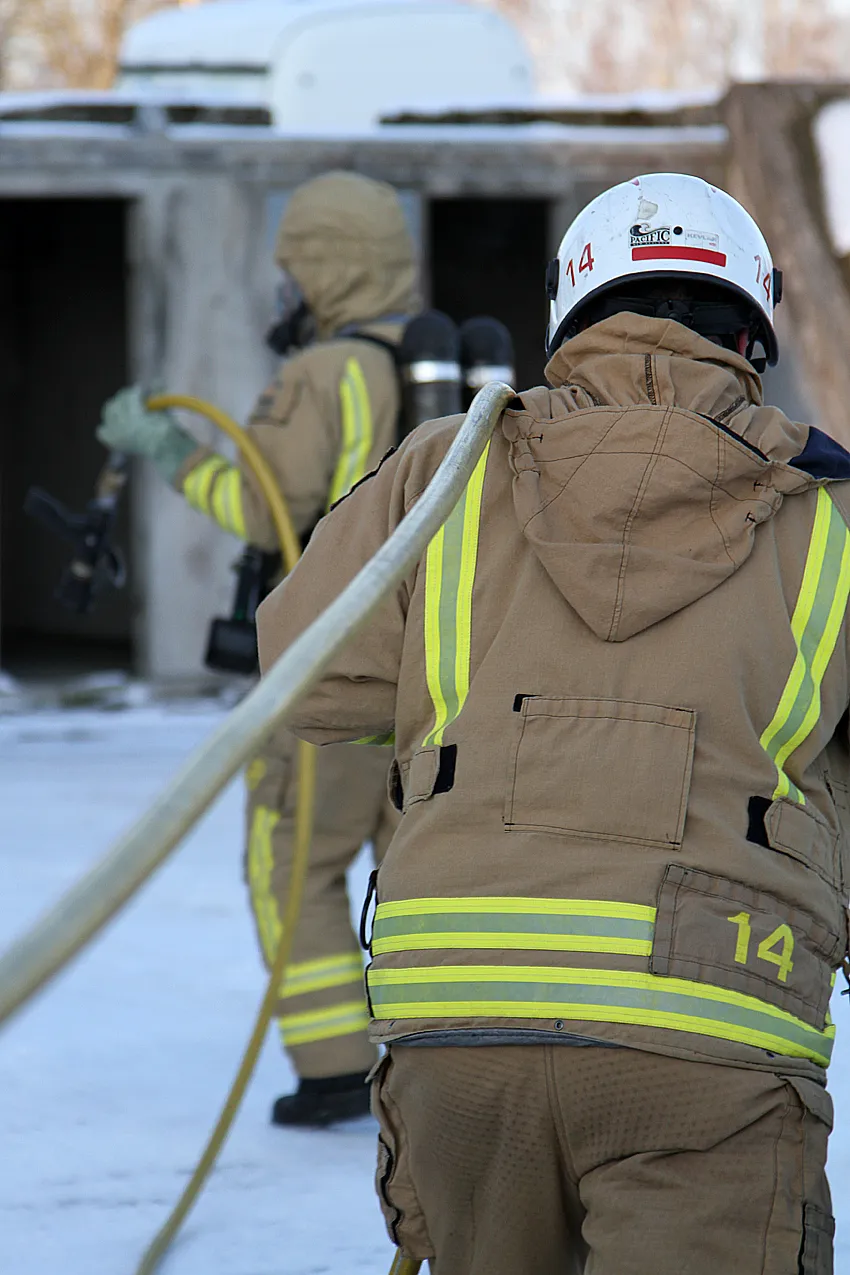 Two firefighters with fire hose in winter landscape during operation