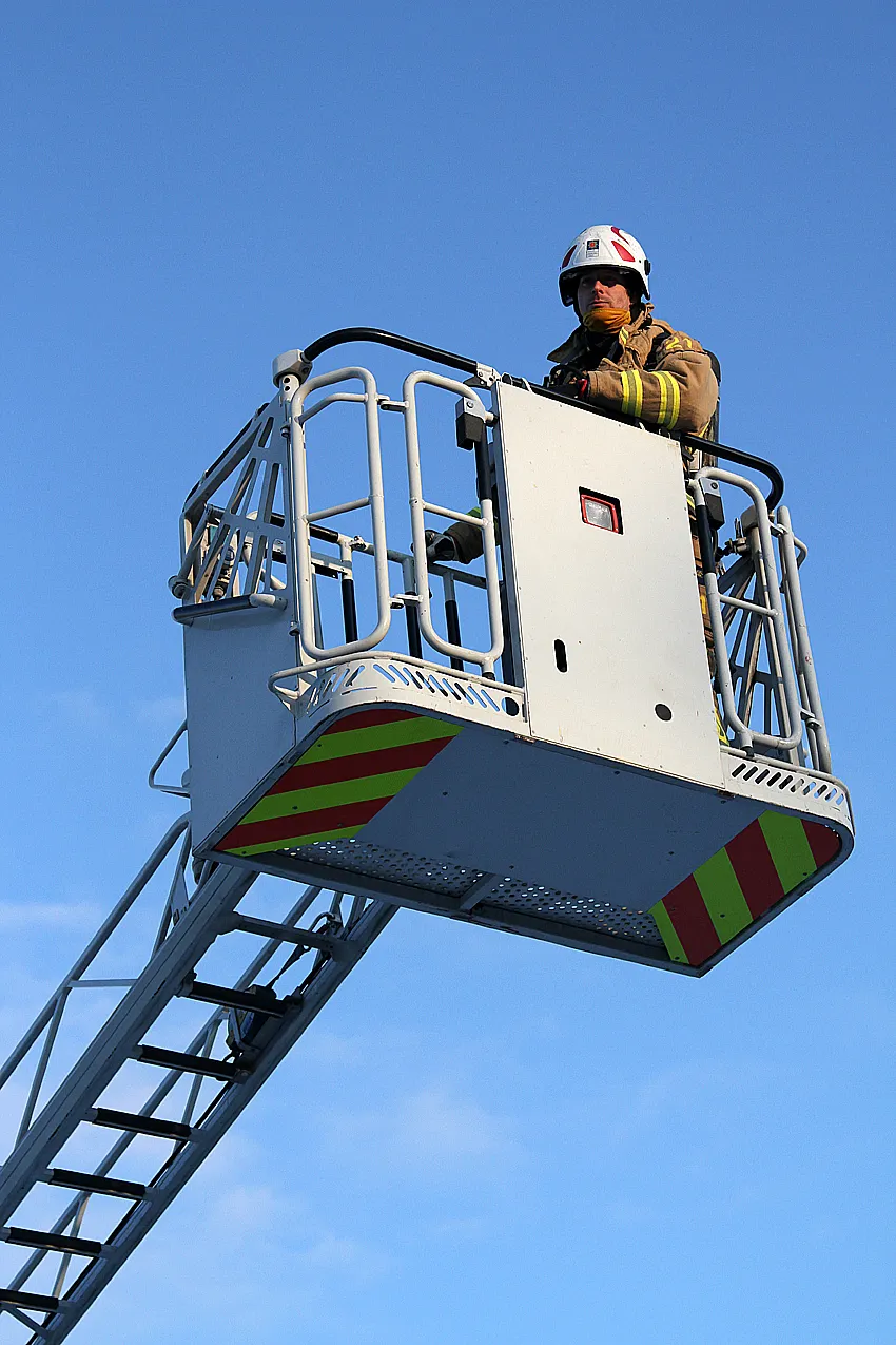 Firefighter in aerial ladder platform basket against blue sky