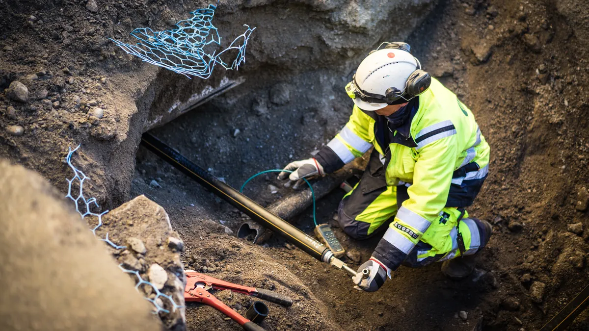 Worker in protective clothing repairing gas pipeline in excavation pit